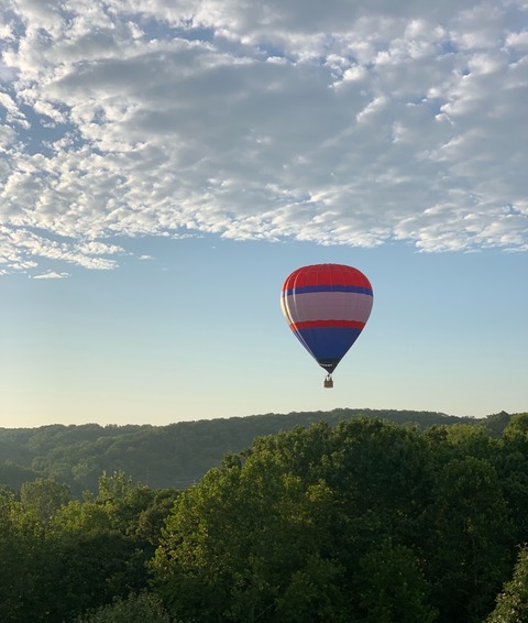 Image of a hot air balloon against a blue sky with clouds above lush, green hills.