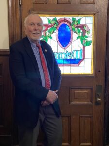 Photos of Tom Braford standing in front of a wooden door with a stained glass window